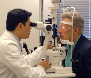 Hombre sentado frente a una lámpara de hendidura para un examen ocular. La barbilla del hombre está apoyada sobre el soporte. El proveedor de atención médica está sentado del otro lado de la lámpara de hendidura y mira a través de los oculares para examinar los ojos del hombre.